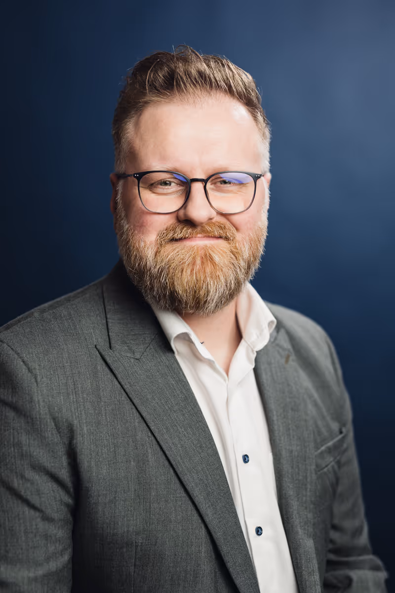 Alexander Herber im grauen Sakko vor blauem Hintergrund