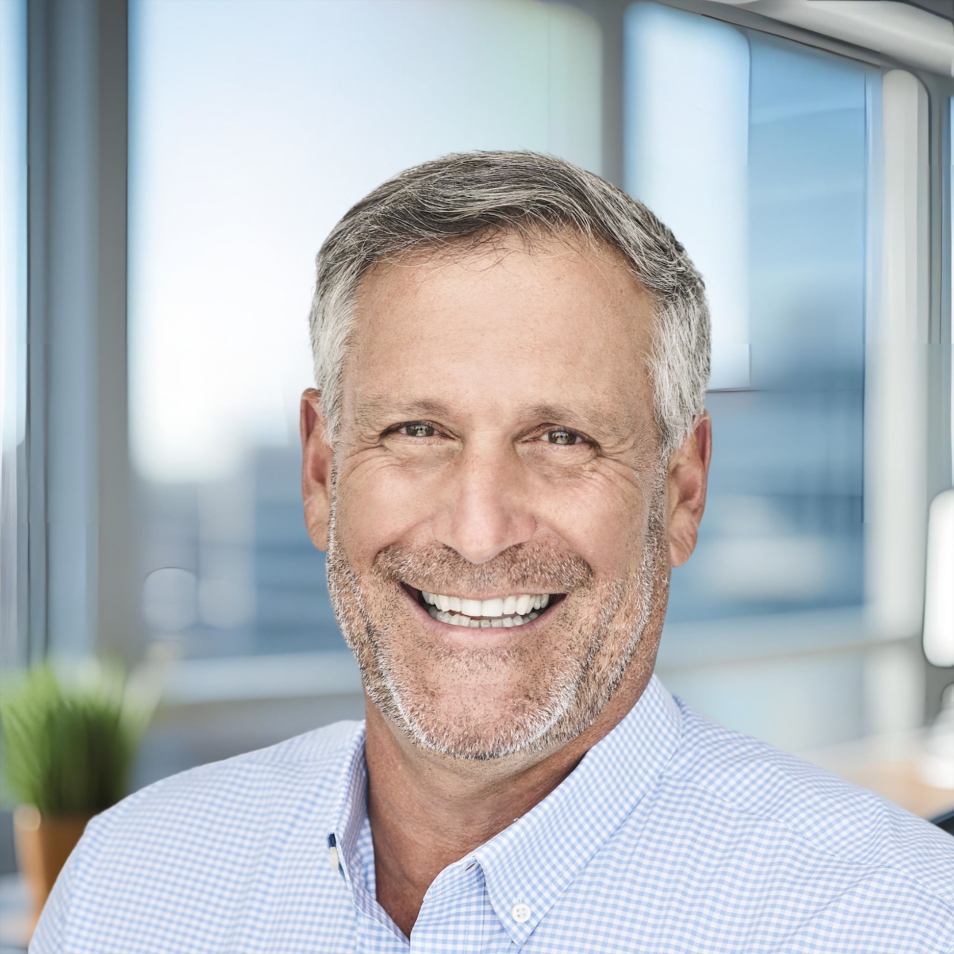 Smiling mature professional in blue checkered shirt near office window