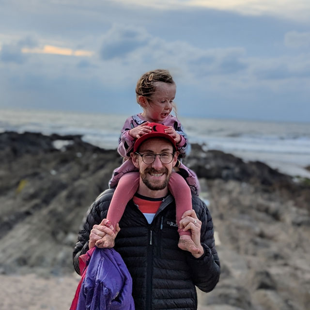 Sam Dockerty walking by the sea with his child on his shoulders