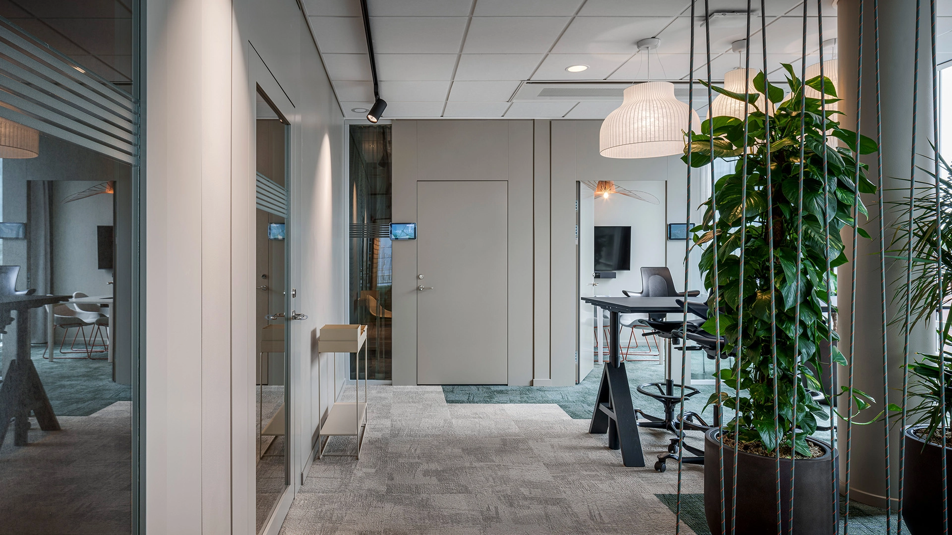 Moderna kontorslokaler med glasväggar, frodiga växter och moderna möbler designade för komfort och produktivitet i en professionell miljö.