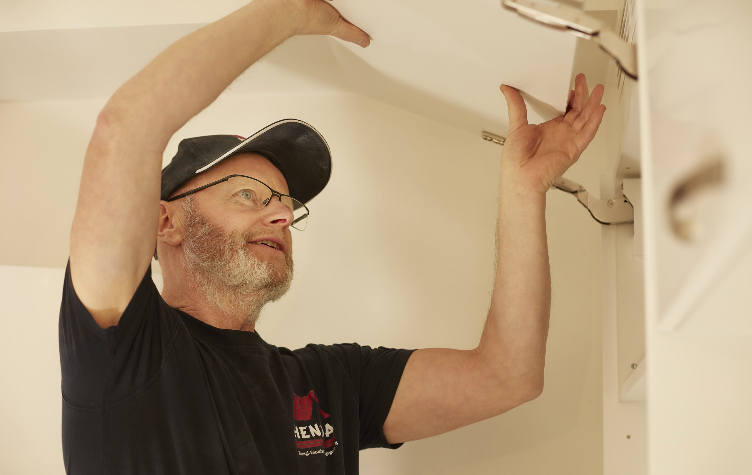 En hantverkare i svart skjorta och keps fokuserar intensivt medan han installerar eller justerar en takarmatur med precision.