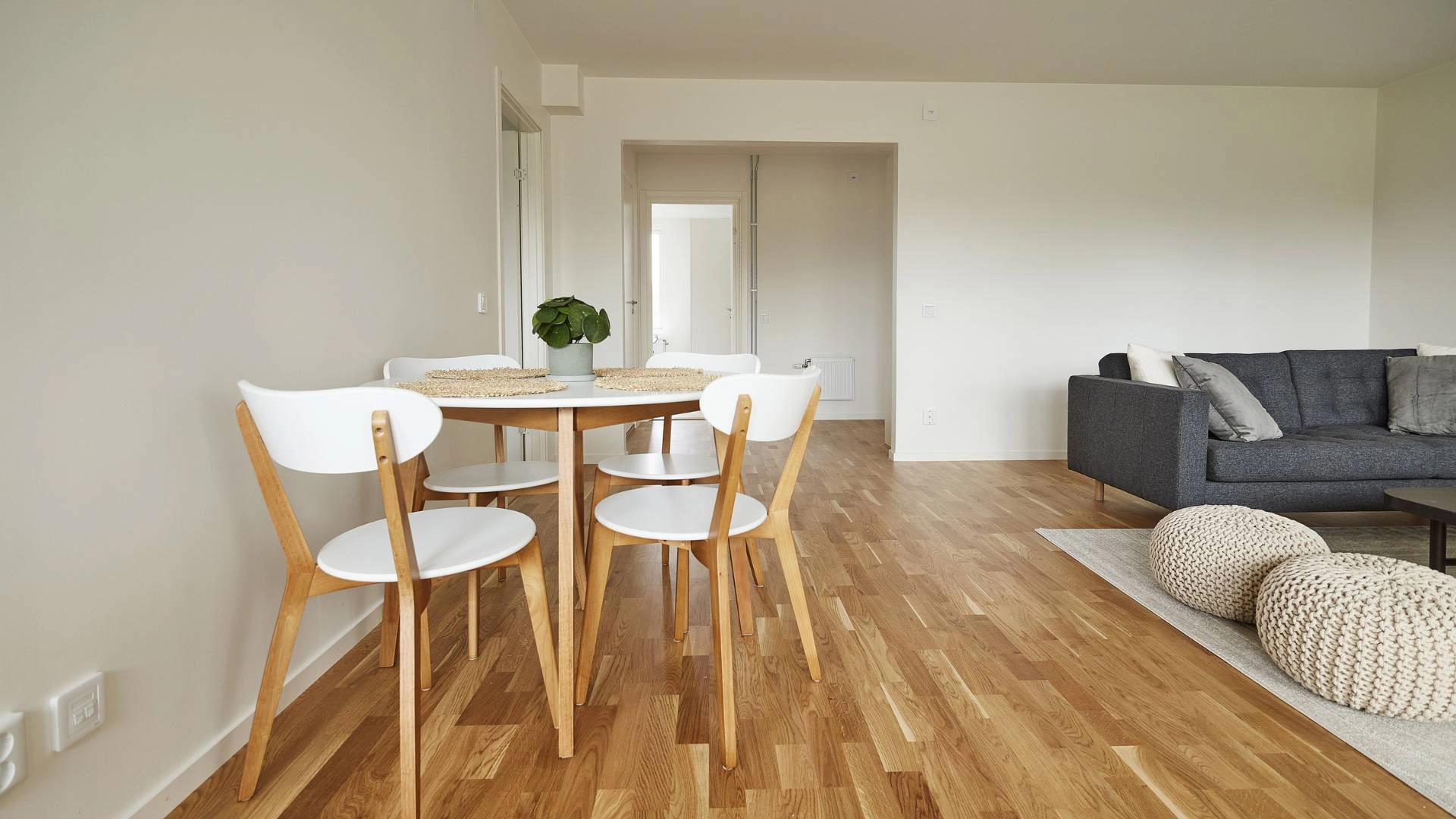 Rymligt modernt vardagsrum och matplats med ett elegant trägolv, rena vita väggar och grå soffmöbler.