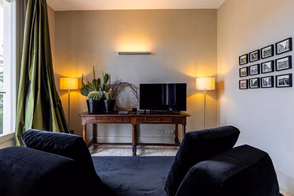Soggiorno moderno con divani neri, scrivania in legno, TV, piante e lampade dorate.