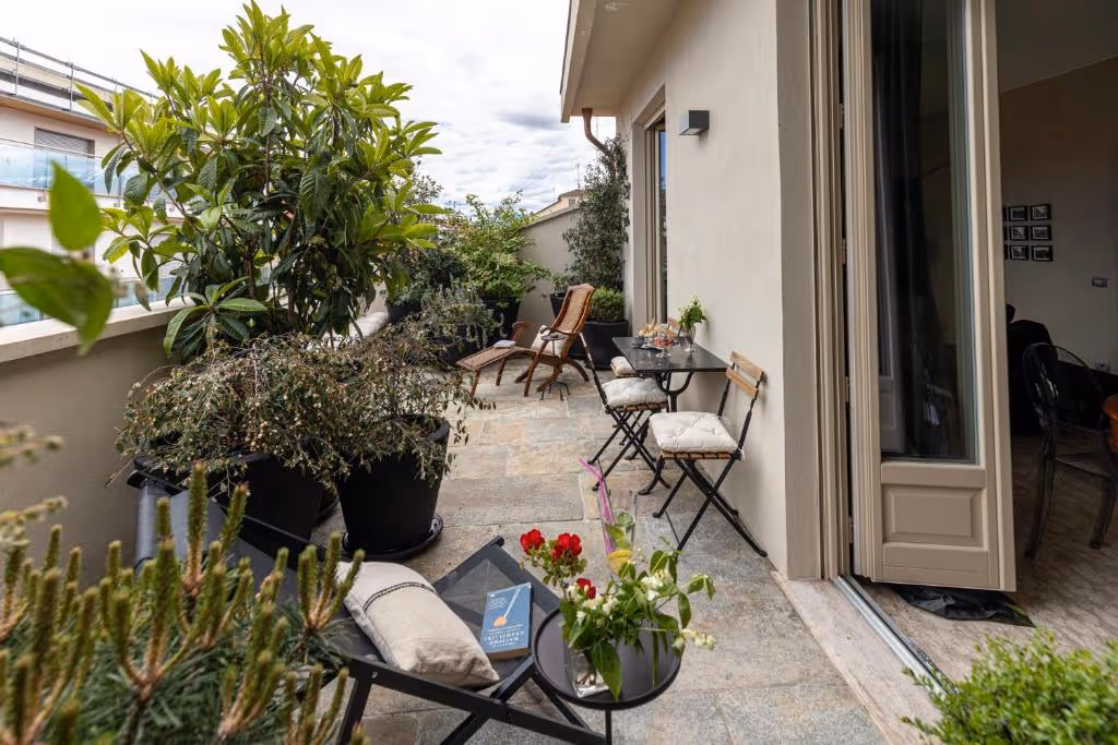 Terrazza moderna con sedie, piante verdi rigogliose e fiori rossi.