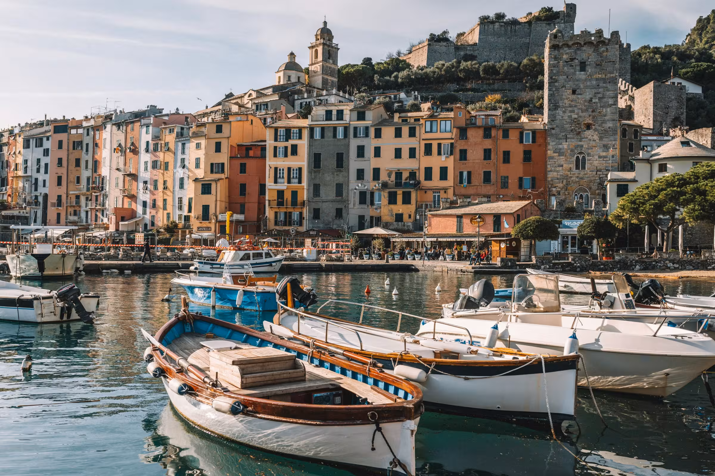 Porticciolo costiero italiano con barche colorate, case variopinte e castello medievale sulle colline