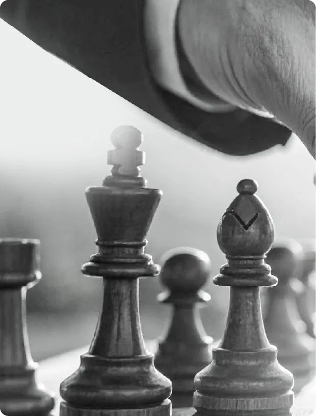 Hand moving a chess piece near a king and bishop on a chessboard in black and white.