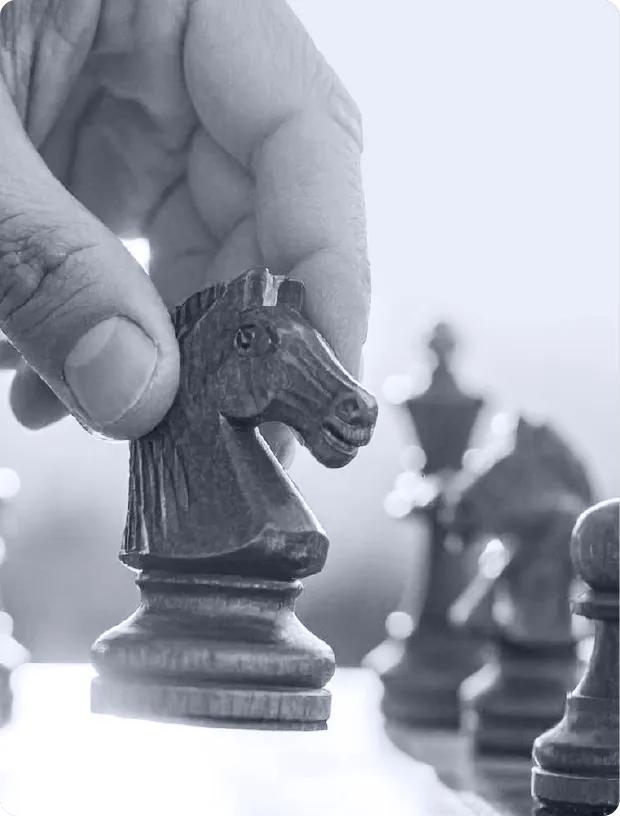 Hand holding a wooden knight chess piece above a chessboard with blurred chess pieces in the background.