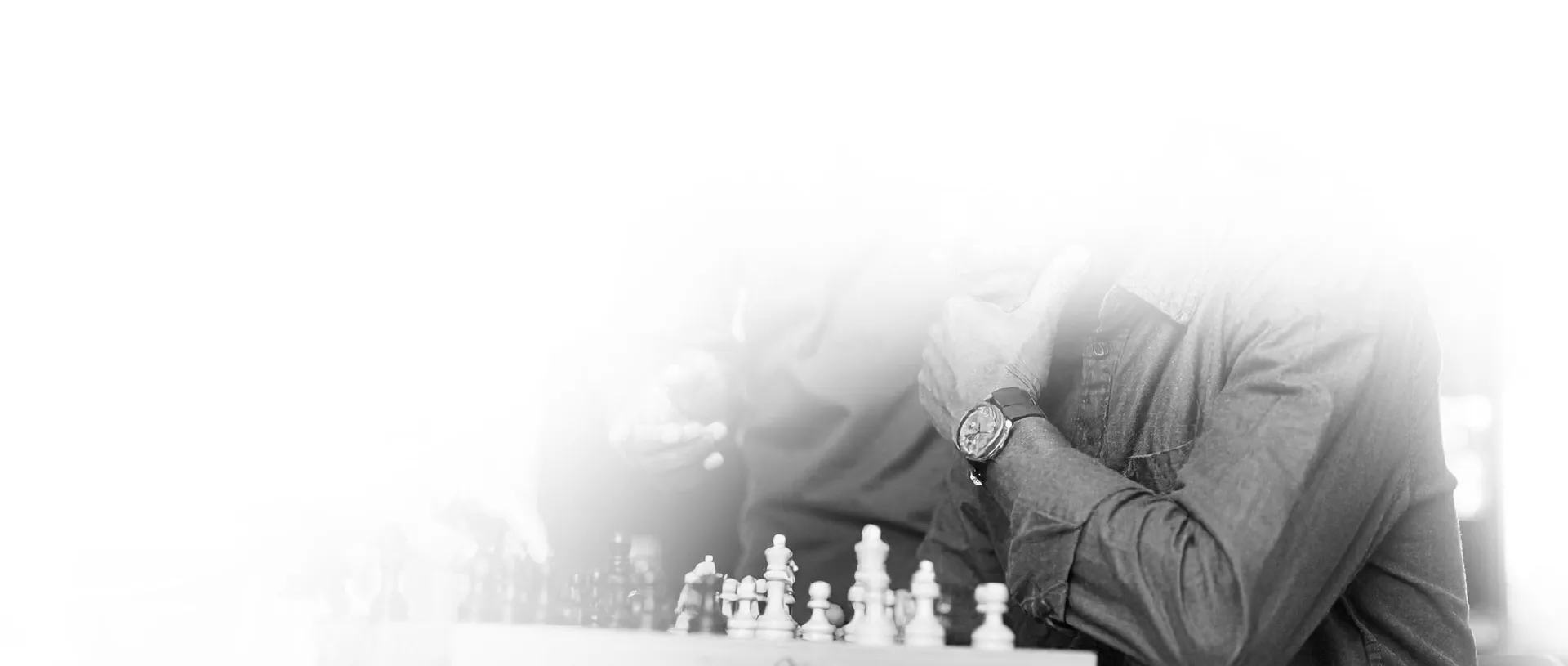 Two people playing chess, one person wearing a watch and a long-sleeve shirt.