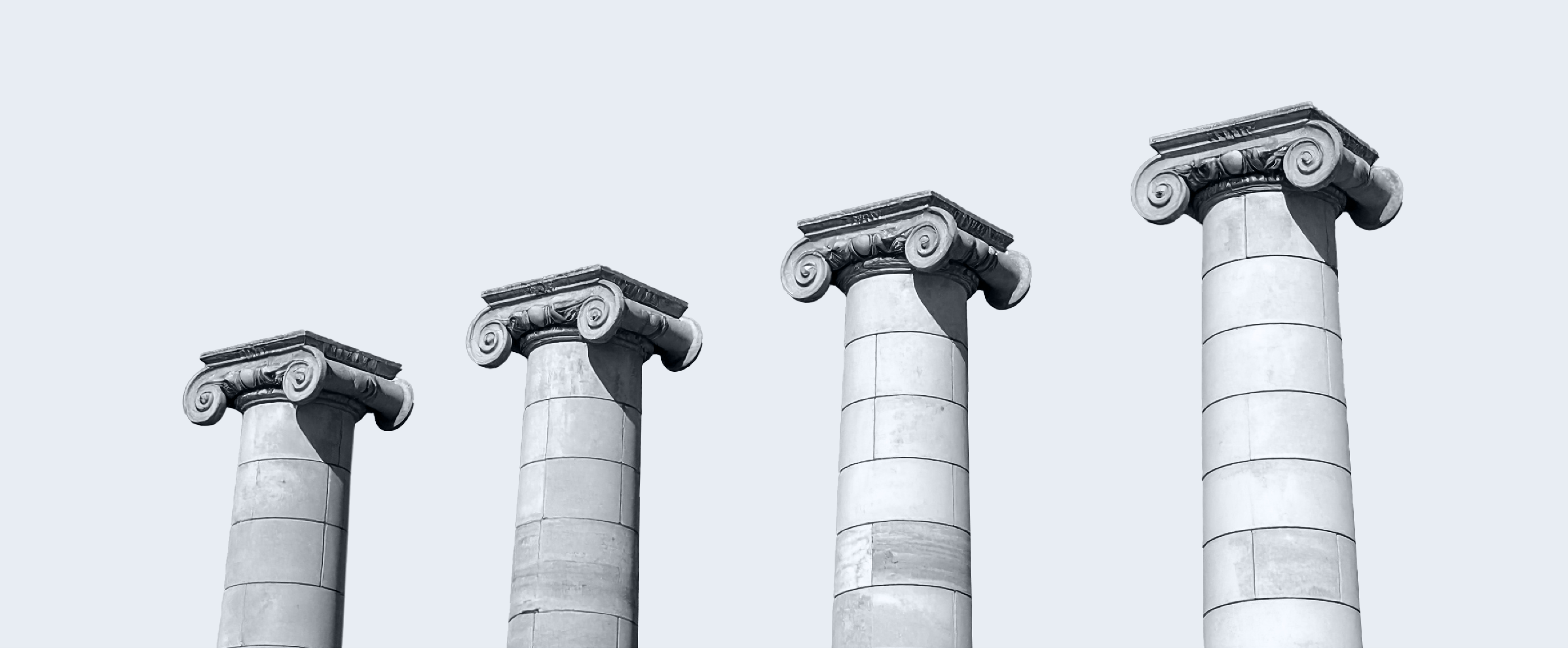 Four classical Ionic columns of varying heights against a pale sky background.