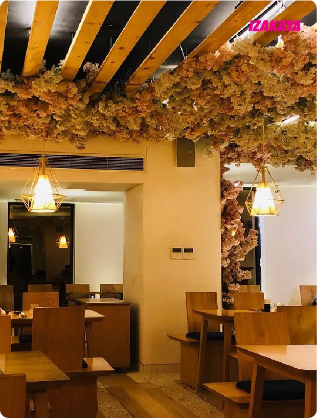 Cozy indoor dining area with wooden tables and chairs, hanging pendant lights, and floral ceiling decor.