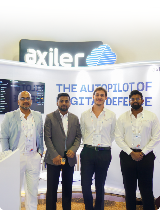 Four men standing in front of an Axiler booth with the text 'THE AUTOPILOT OF DIGITAL DEFENSE'.