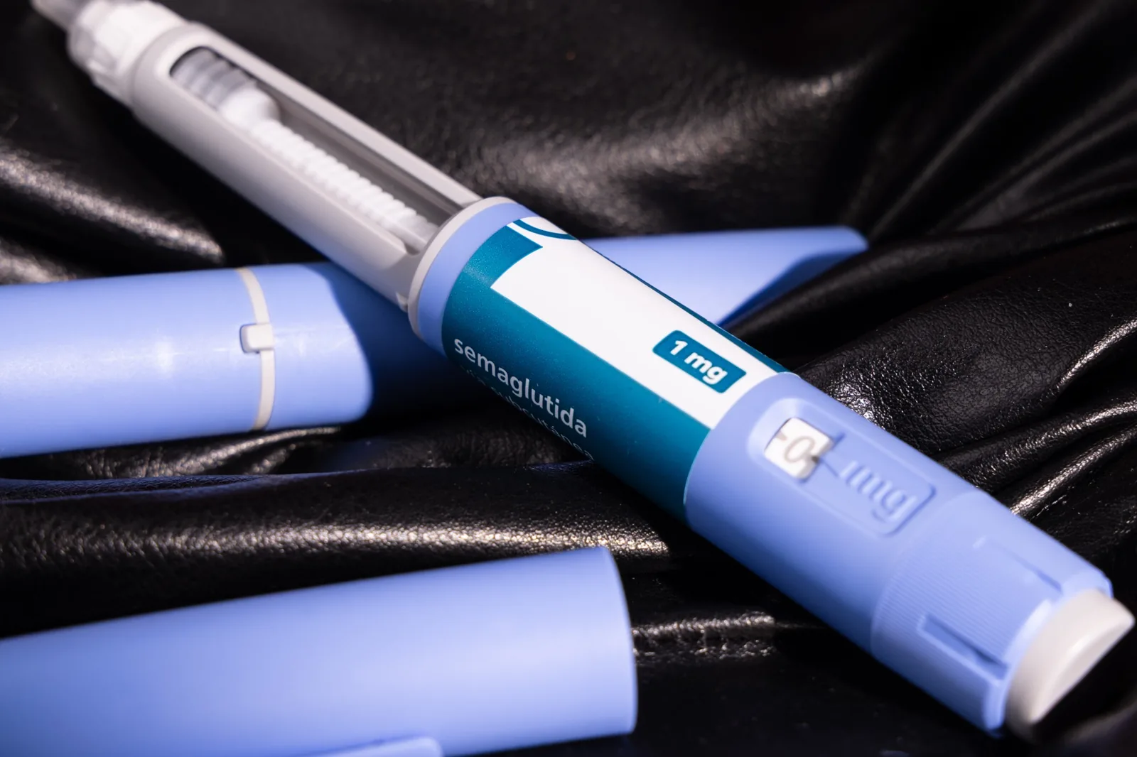 Semaglutide injection pen with 1 mg dosage on blue casing against a black leather background.