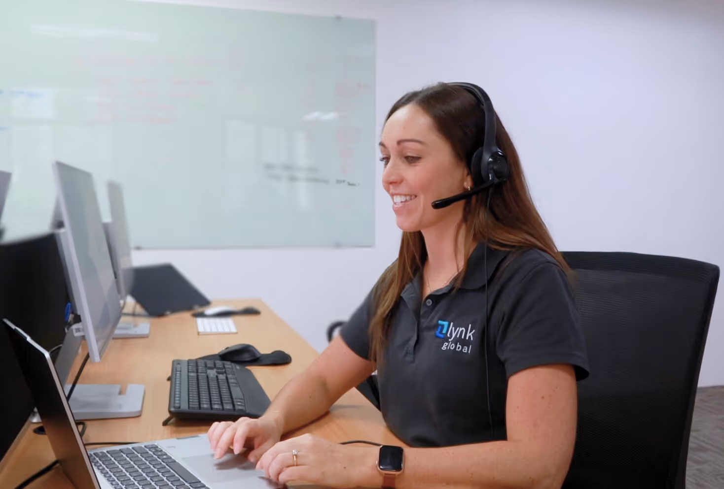 Smiling Lynk Global team member wearing a headset at her desk, assisting a client request.