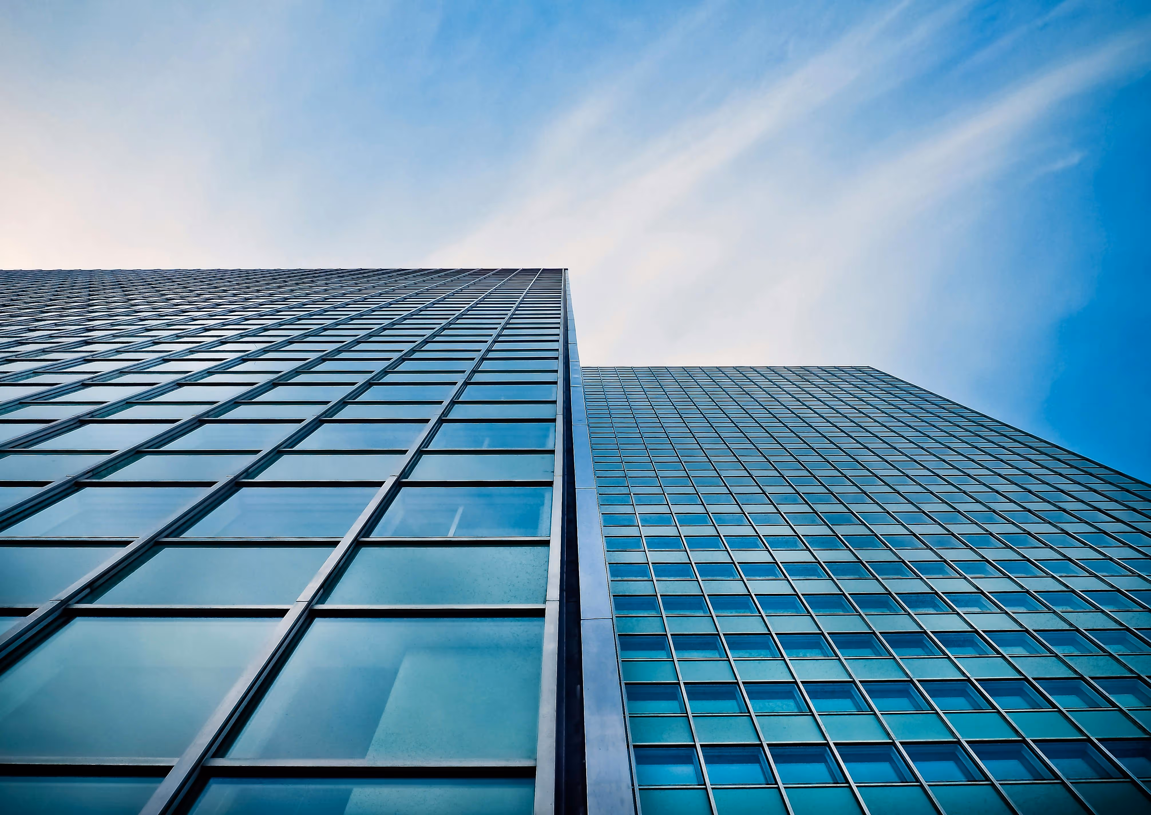 Upward view of modern glass office buildings against a blue sky, used as background for Lynk Global client testimonials
