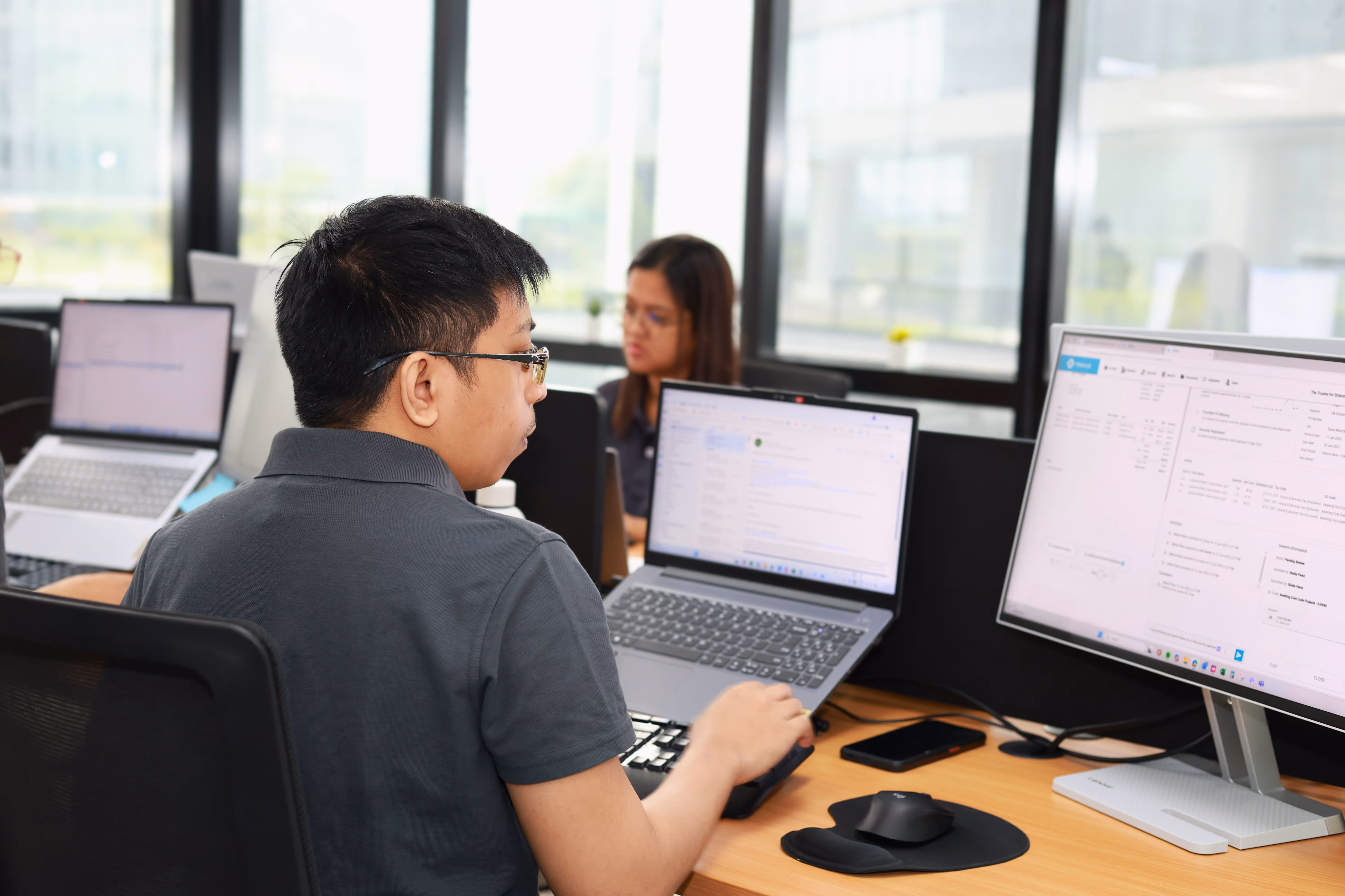 Lynk Global staff member reviewing payroll data and employee records on dual screens in a managed office environment