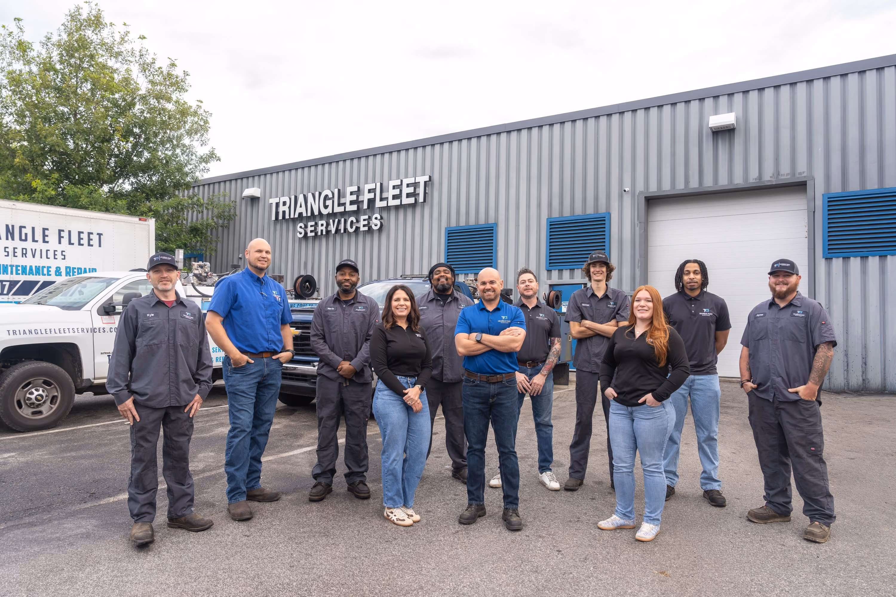 Group of eleven diverse employees standing outside a building labeled Triangle Fleet Services.