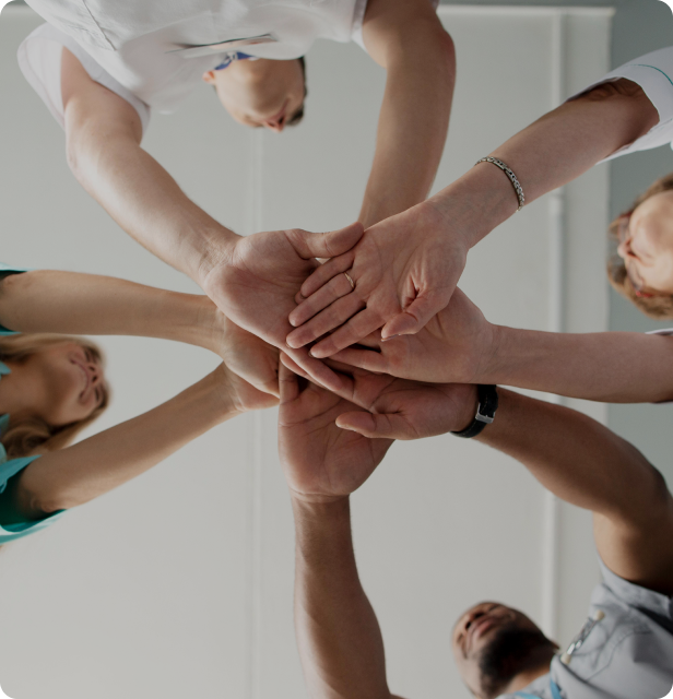 A group of medical professionals with their hands stacked in a gesture of teamwork and commitment.