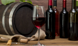 A still life composition of wine bottles, a glass of red wine, and a barrel.