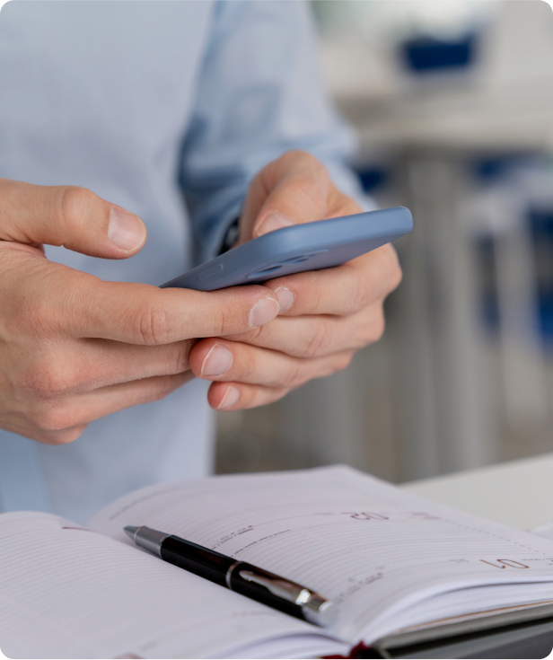 Person holding a smartphone with a notebook and pen on the table.