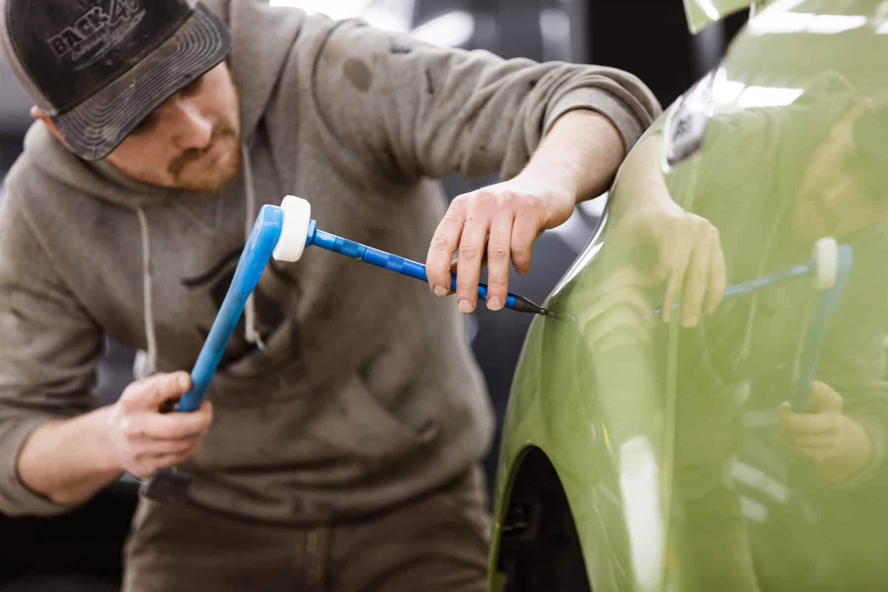 A man fixing the side of the car's body exterior.