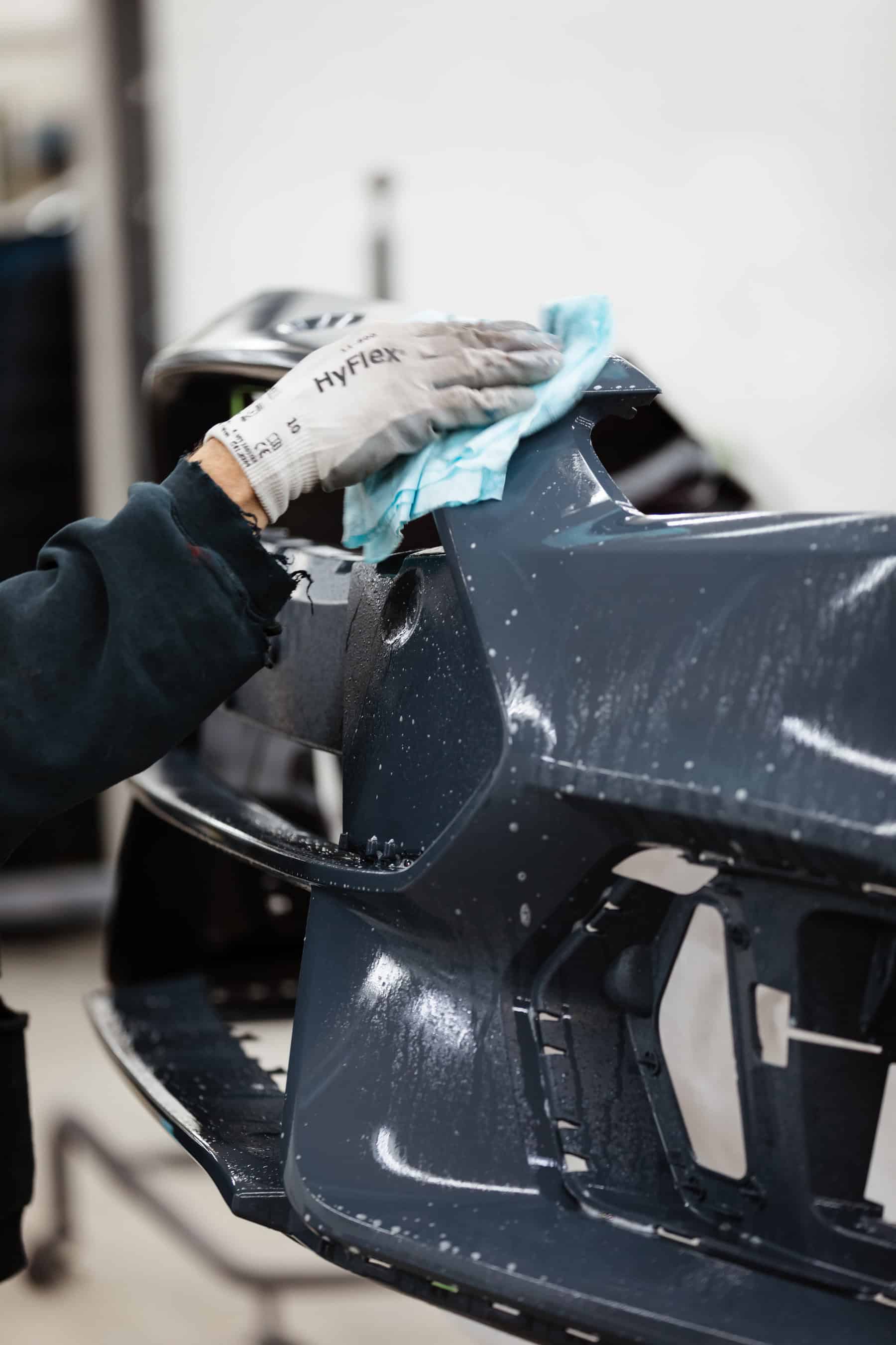 A man in a black jacket and gloves polishing a car.