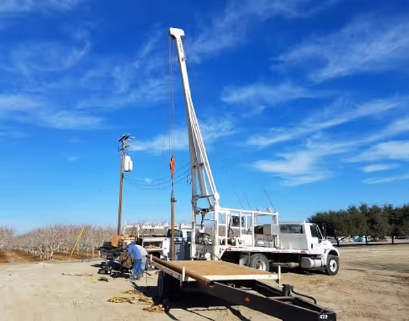 Truck-mounted crane working in orchard with utility pole and blue sky