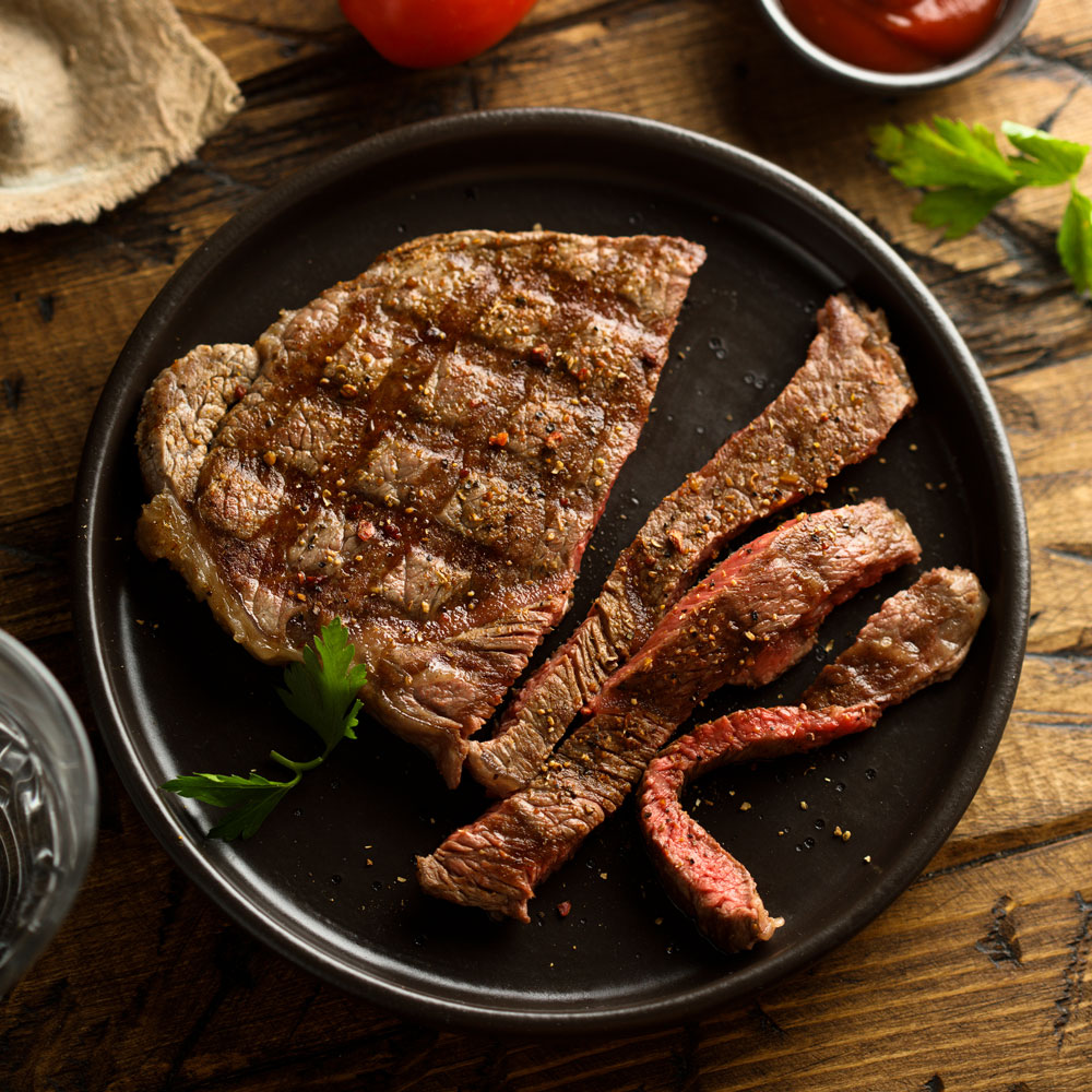 A plate of steak with tomatoes and peppers on a wooden table.