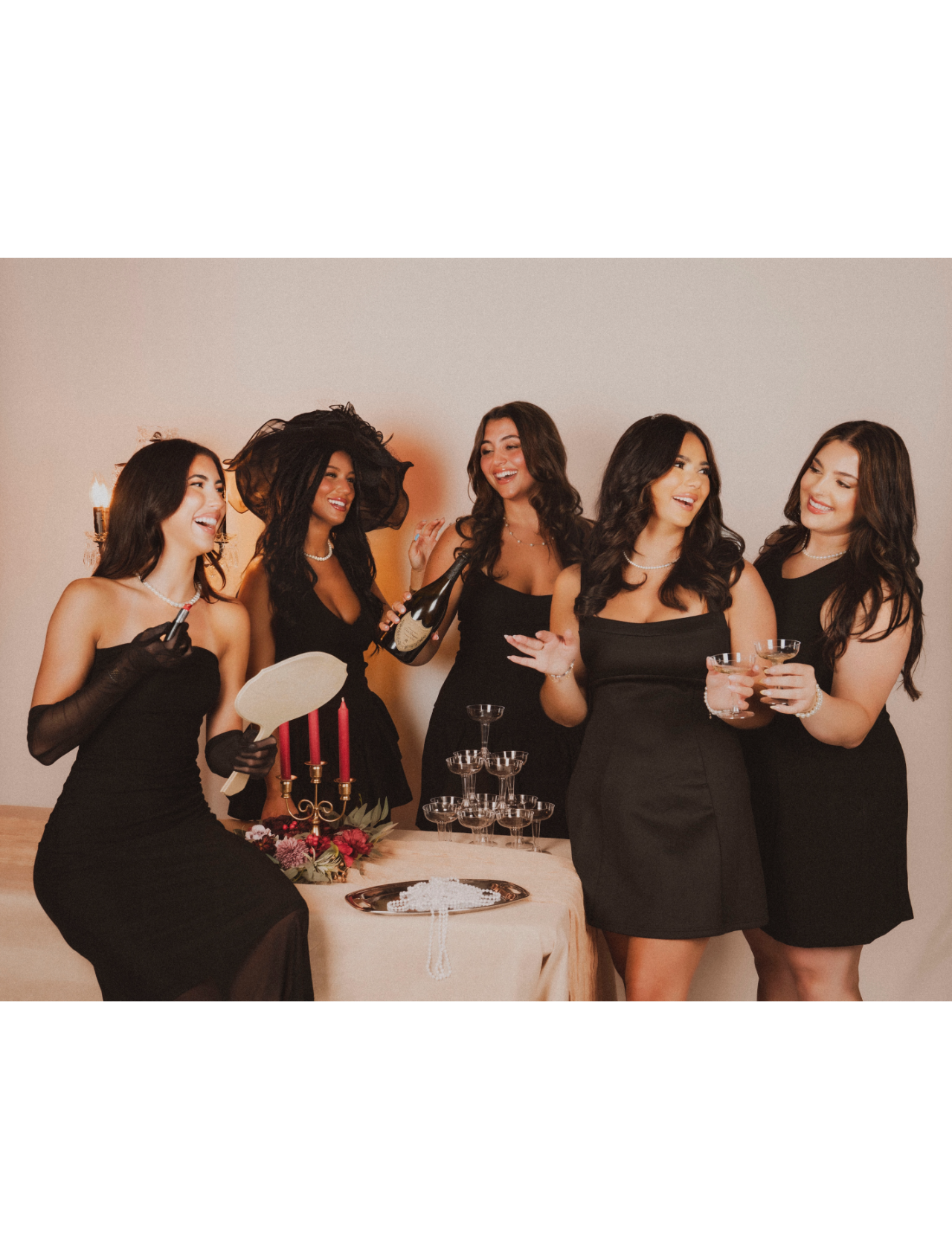 A fun image of 5 of Razberri's Salon's stylists all dressed in black dresses, smiling and toasting with champagne glasses.