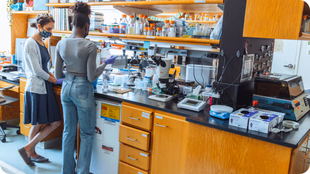 Two women standing in a scientific lab holding pipets and wearing masks