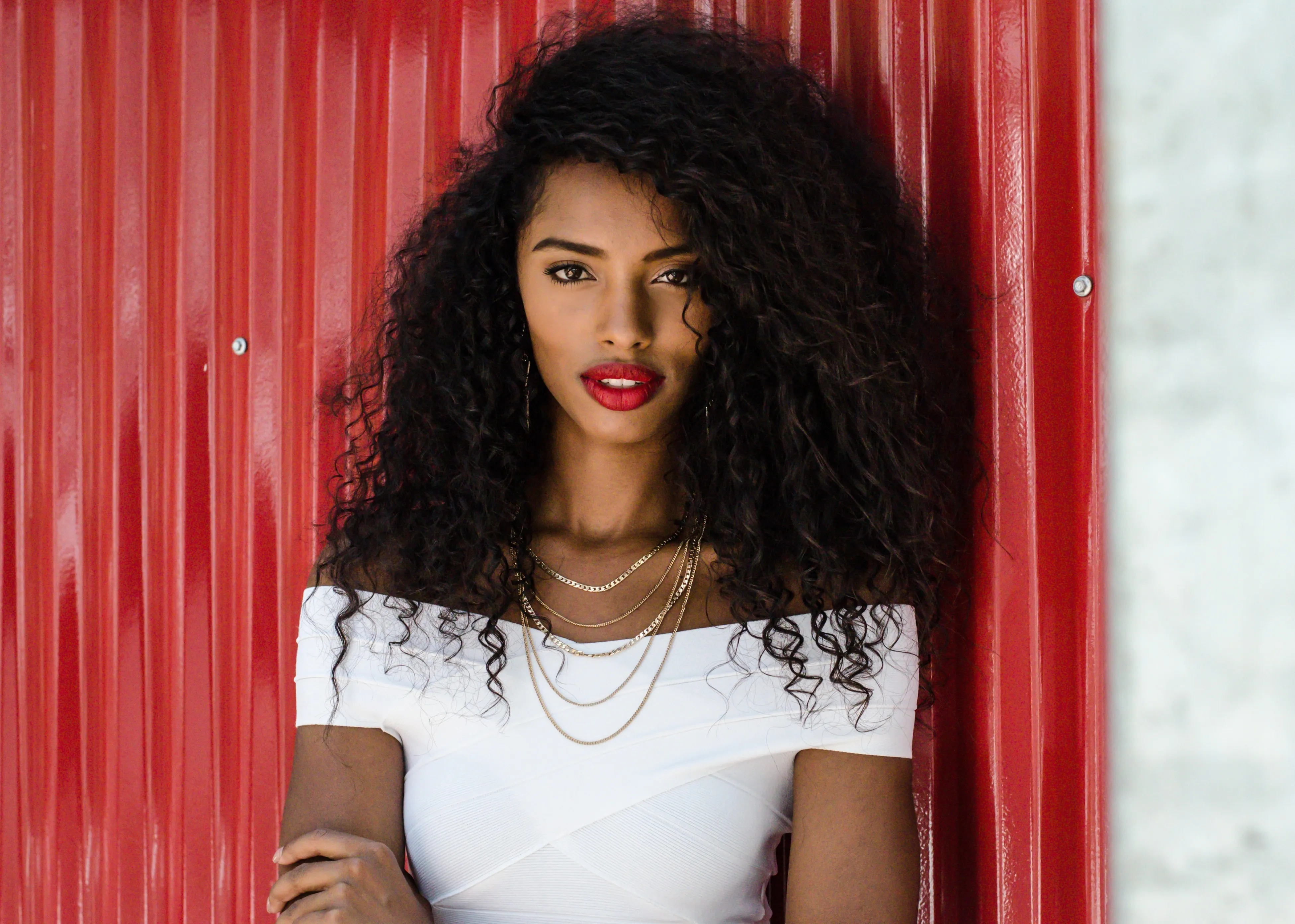 A woman with long curly hair standing in front of a red wall.