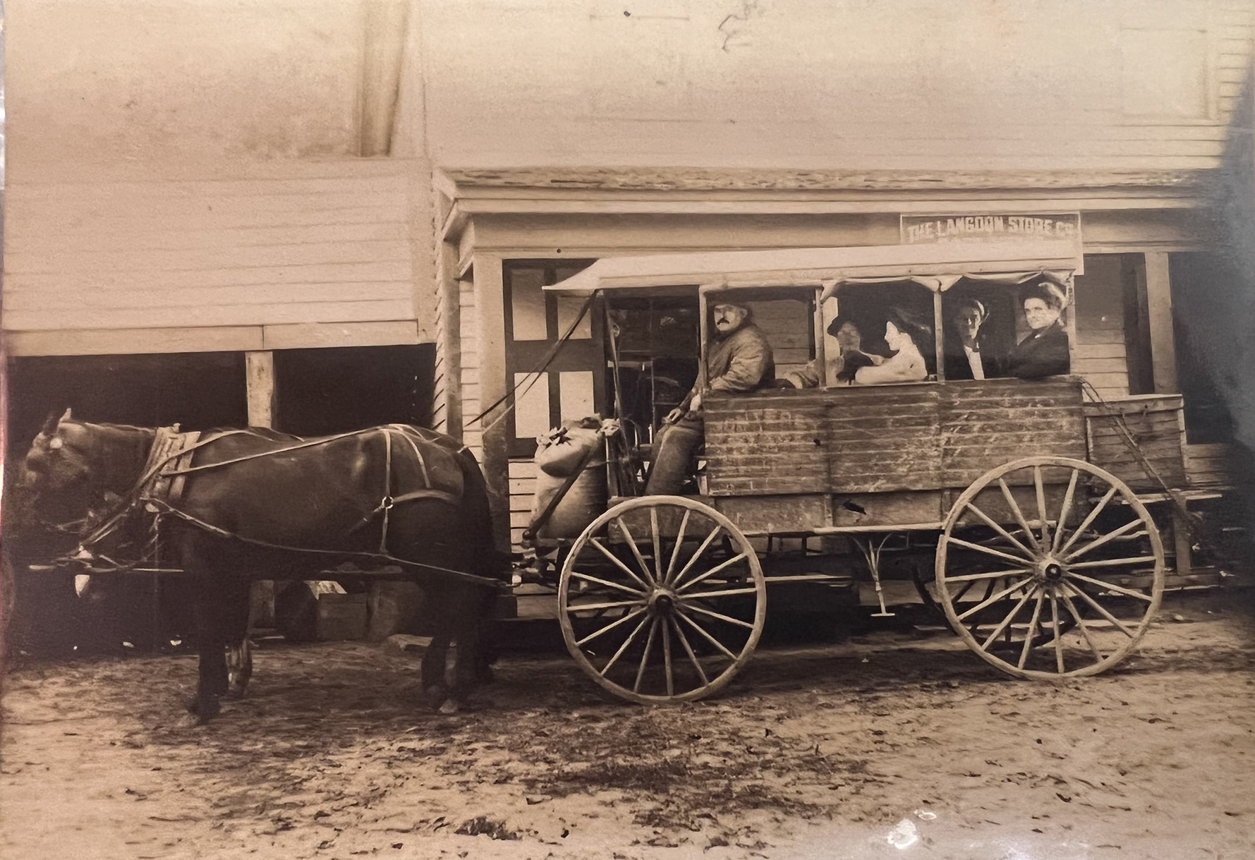 Historic image of the Monterey Stage Wagon circa 1900, with passengers seated in front of the Langdon Store in Monterey, Massachusetts.