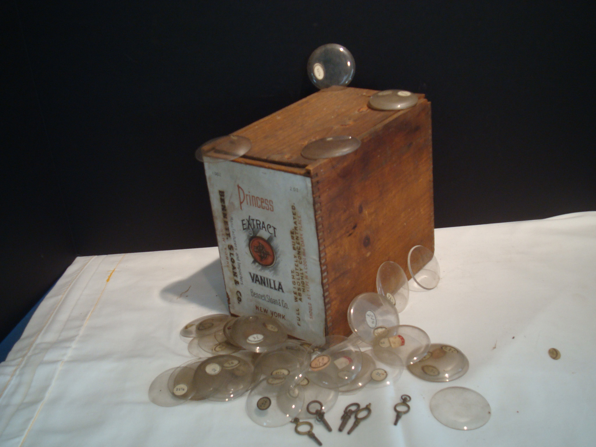 Box containing Princess Extract Vanilla alongside small glass watch crystals and metal stem winders, showcasing personal and commercial artifacts from historic Monterey, Massachusetts.