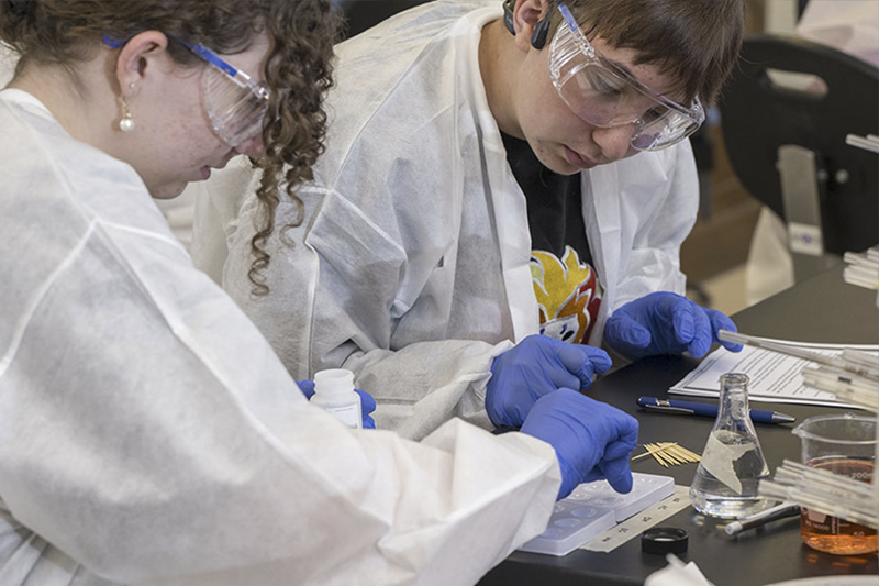 Student works at a computer and looks toward 3d printer.