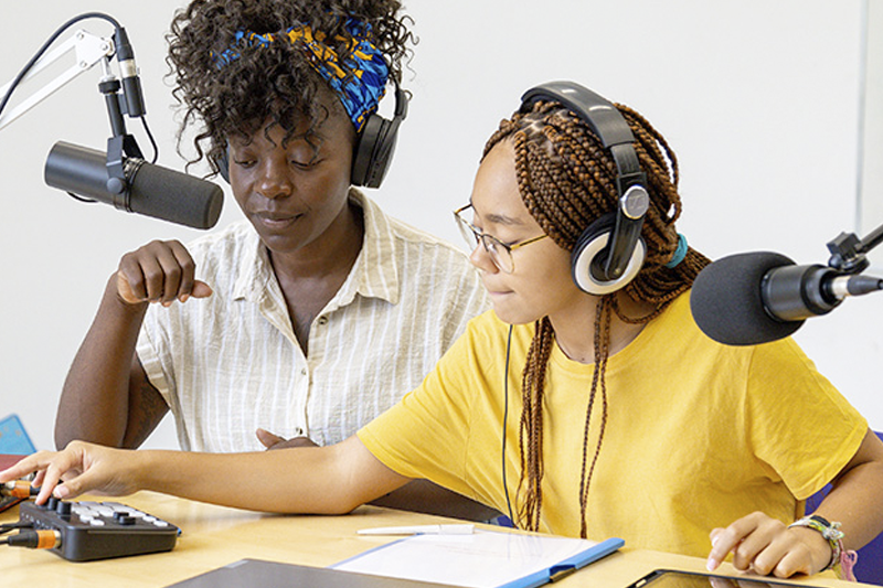 Student works at a computer and looks toward 3d printer.
