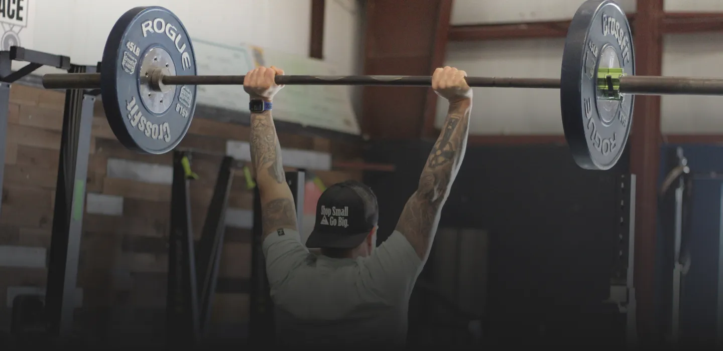 An image of the back of a man holding a barbell over his head at a group fitness class at a gym in Newtown, CT.