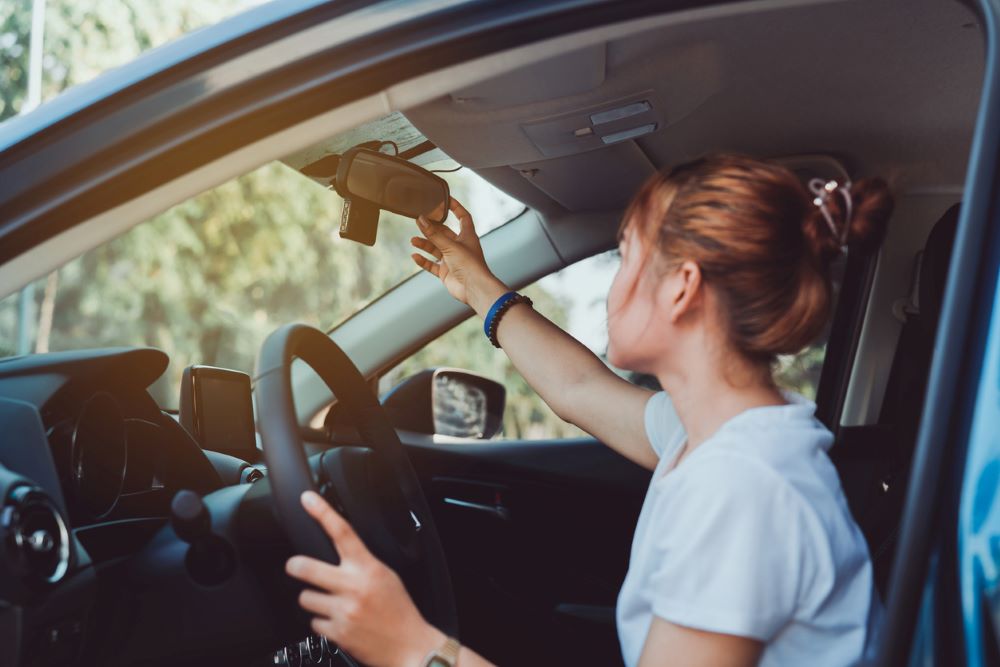 A woman is sitting inside a car and is adjusting her mirror.|