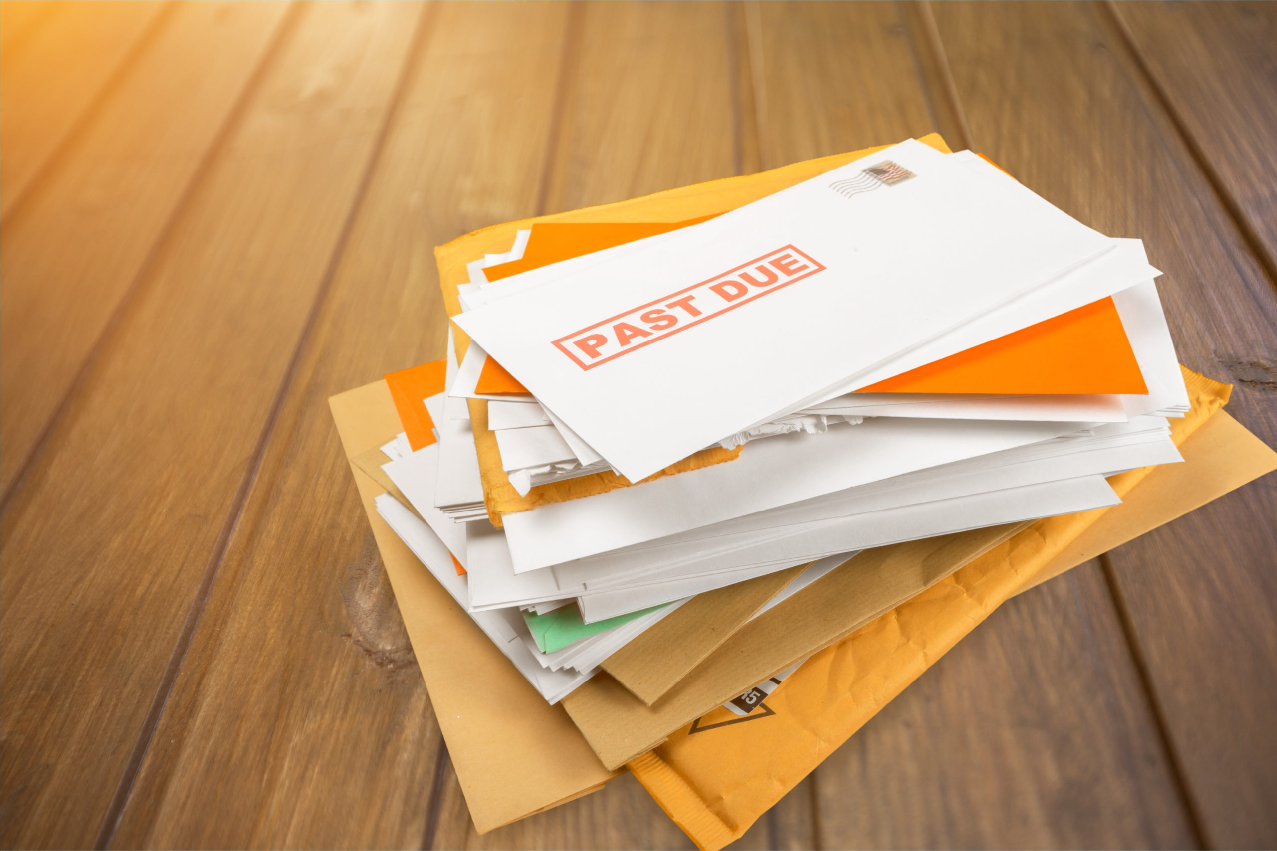 Stack of bills and mail on wooden table.