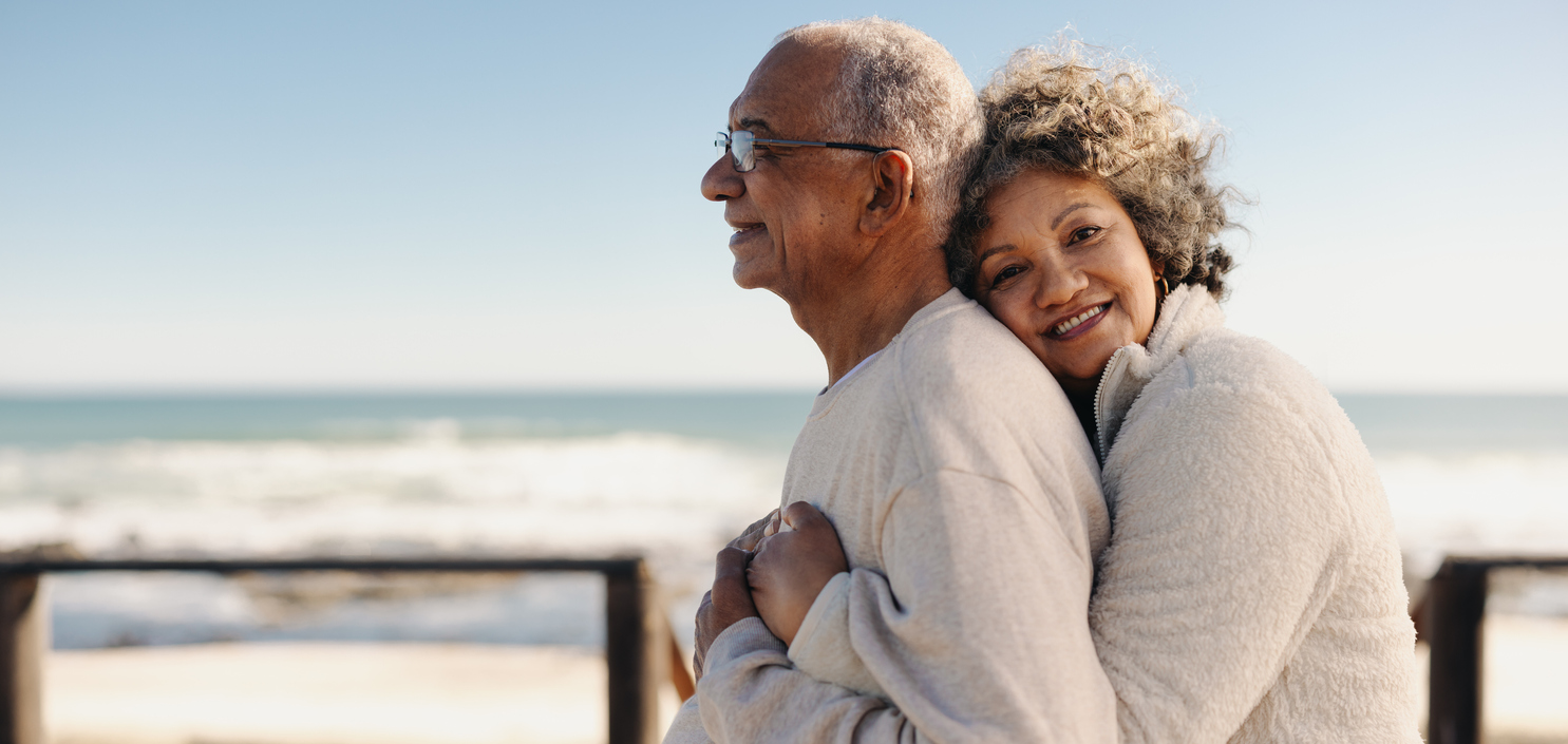 Romantic senior woman embracing her husband by the ocean.