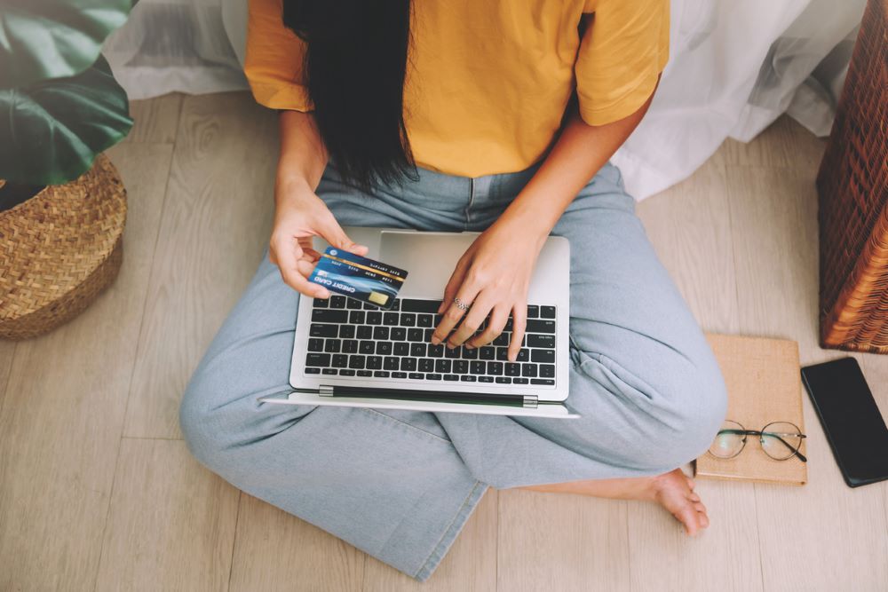 Asian woman freelancer wearing yellow t-shirt using credit card and laptop.