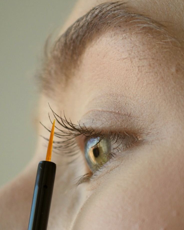 a close up photo of woman applying serum to eyelashes