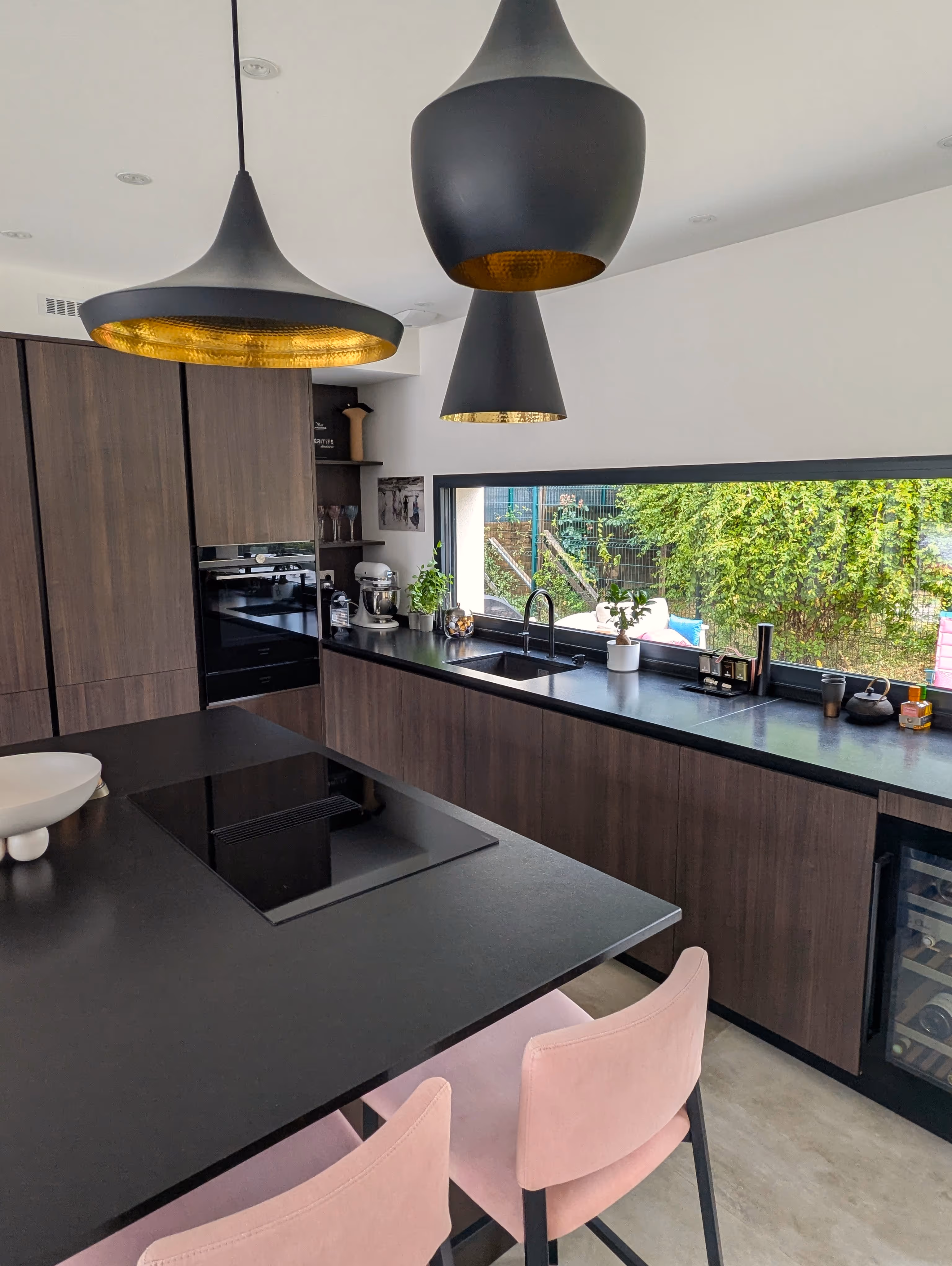 Cuisine rénovée avec meubles en bois foncé, plan de travail noir et suspensions dorées, projet Cocoon à Grenoble