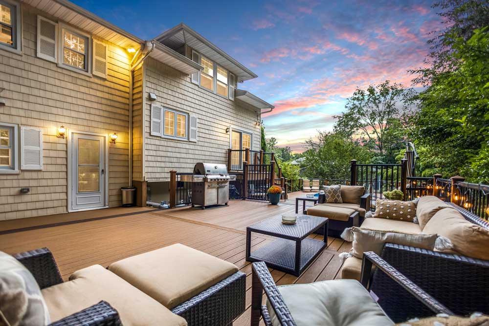 Twilight real estate photo of a large outdoor deck with patio seating and a grill, perfect for marketing outdoor living spaces.
