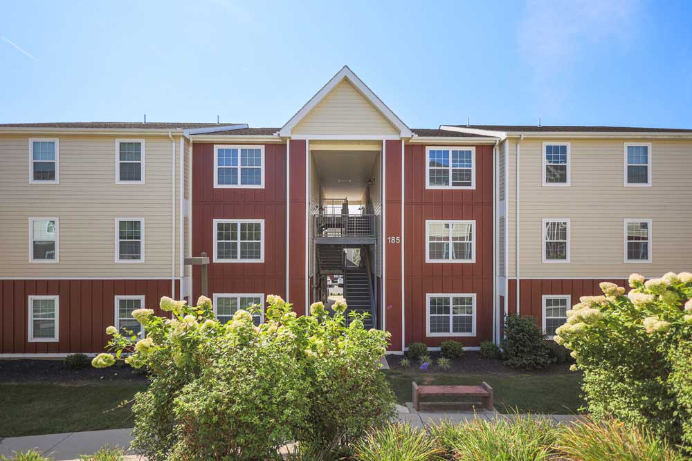 Exterior photo of a red and beige multi-unit townhome with lush landscaping, captured for real estate listing photography.