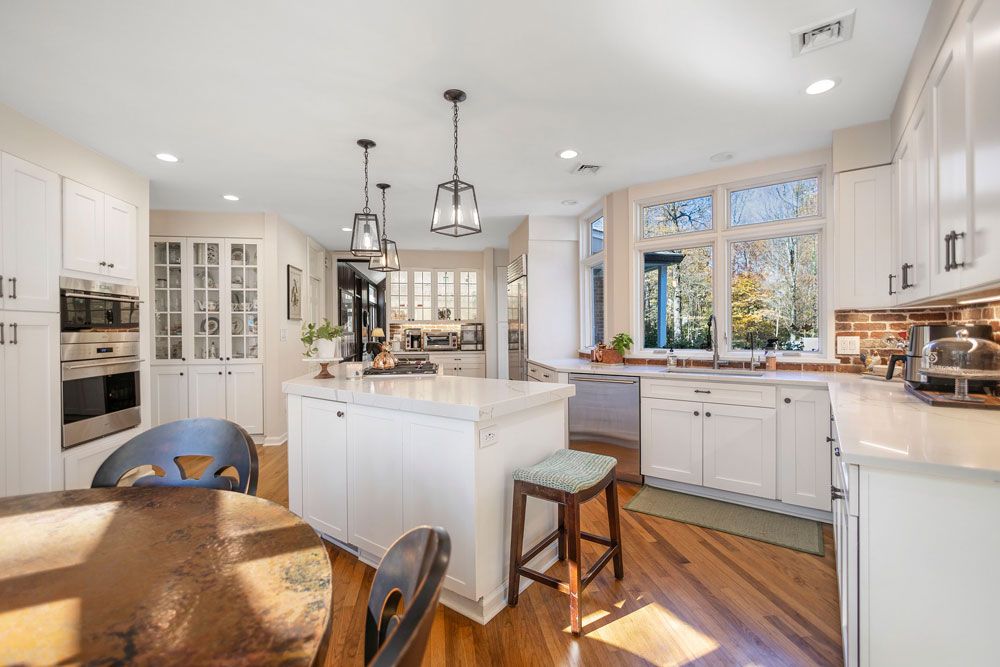Bright and modern kitchen with white cabinets, island seating, and wood flooring, professionally photographed for real estate marketing.