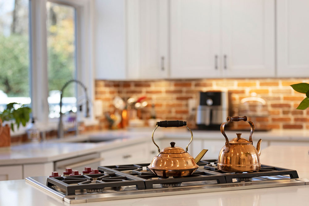Close-up of copper tea kettles on a gas stove in a luxury kitchen, ideal detail shot for real estate listing photography.