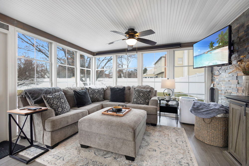 Bright and cozy sunroom with sectional couch and mounted TV, featured in real estate marketing photography.