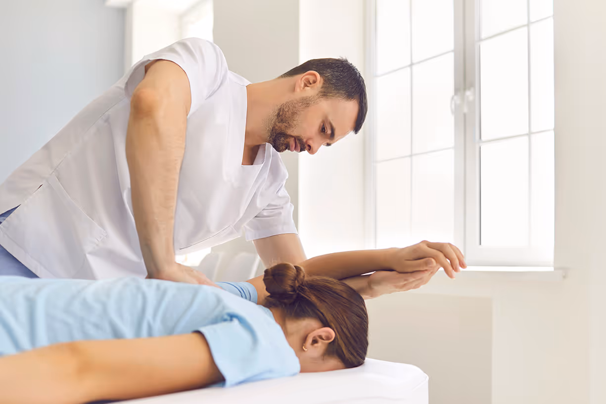 a man standing over a woman on a massage table. The man is raising the woman's arm over her head into a deep stretch