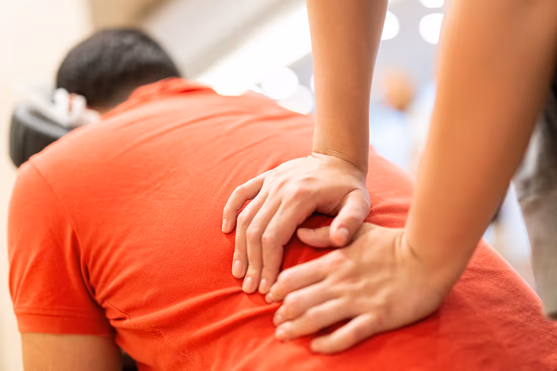 A man in a red shirt lying down on a massage chair while a man massages his back