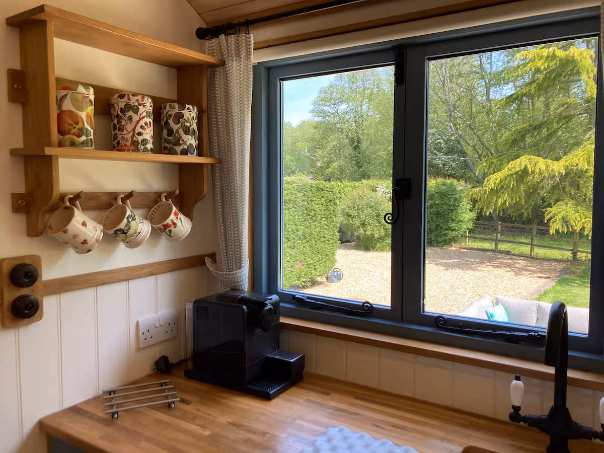 Kitchenette worktop beneath the window, with a Nespresso machine, hanging mugs and sink tap.
