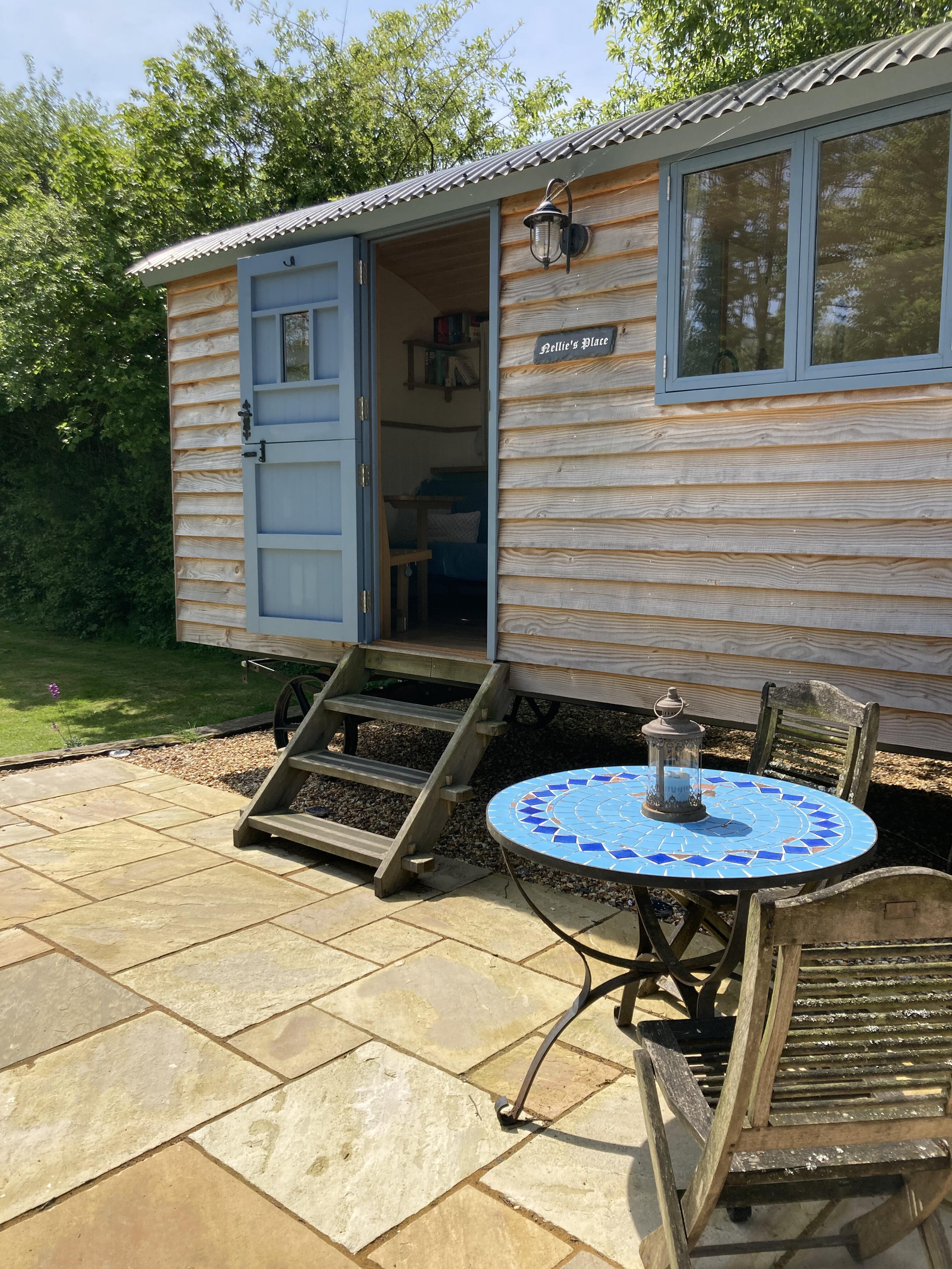 External wooden steps leading from the paved patio to the hut’s open blue entrance door.